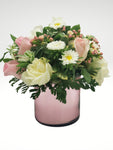 Coqueto arreglo floral compuesto por hermosas rosas, en tonos rosa y blanco acompañadas por margaritas que logran un efecto de gran sutileza. Recomendado para demostrar un amor lleno de ternura y romanticismo.  Especificaciones del Arreglo: Follaje, Cilindro de vidrio color rosa tornasol Incluye Mensaje impreso, Altura promedio del arreglo: 30 - 35 cm.