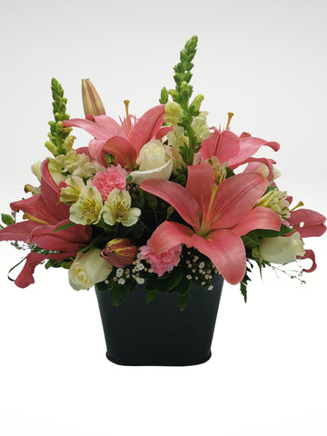 Sofisticado arreglo floral compuesto por hermosas rosas blancas, lilies rosas, lirios y boca de dragón para dar un toque de glamour y elegancia. Es una opción ideal para enviar un regalo a una persona con estilo. Base metálica color negro, Incluye mensaje impreso, Altura promedio del arreglo: 45 cm