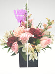 Lindo arreglo floral tamaño "petite" compuesto por rosas y claveles en tonos rosa. Es el diseño ideal combinarlo con otras sorpresas!  ESPECIFICACIONES DEL ARREGLO:  Follaje Cubo de madera Incluye dedicatoria Altura promedio del arreglo: 30 cm