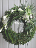 Discreto y elegante diseño de corona floral con transiciones florales y en follaje. Corona fúnebre con elegantes flores en color blanco y follaje en tonos verde sobre tripie de herrería. Altura final promedio: 1.70 cms. El tono de las flores y el follaje puede variar de acuerdo a la disponibilidad. Incluye listón personalizado.