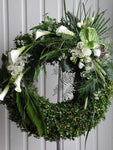 Discreto y elegante diseño de corona floral con transiciones florales y en follaje. Corona fúnebre con elegantes flores en color blanco y follaje en tonos verde sobre tripie de herrería. Altura final promedio: 1.70 cms. El tono de las flores y el follaje puede variar de acuerdo a la disponibilidad. Incluye listón personalizado.