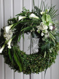 Discreto y elegante diseño de corona floral con transiciones florales y en follaje. Corona fúnebre con elegantes flores en color blanco y follaje en tonos verde sobre tripie de herrería. Altura final promedio: 1.70 cms. El tono de las flores y el follaje puede variar de acuerdo a la disponibilidad. Incluye listón personalizado.