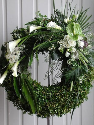 Discreto y elegante diseño de corona floral con transiciones florales y en follaje. Corona fúnebre con elegantes flores en color blanco y follaje en tonos verde sobre tripie de herrería. Altura final promedio: 1.70 cms. El tono de las flores y el follaje puede variar de acuerdo a la disponibilidad. Incluye listón personalizado.
